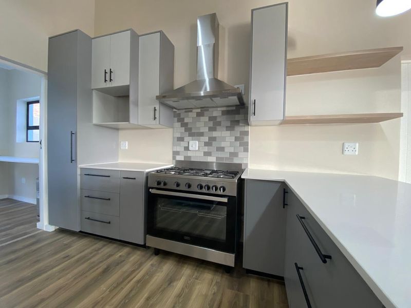 Modern kitchen featuring grey cabinetry, white quartz countertops, stainless steel gas stove with extractor fan, and stylish subway tile backsplash.