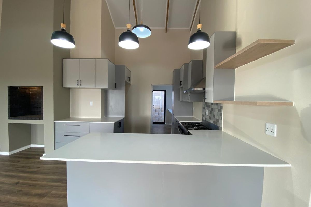 Modern kitchen featuring sleek grey cabinetry, stone countertops, built-in appliances, and a feature fireplace, set within an open-plan living space with high ceilings.