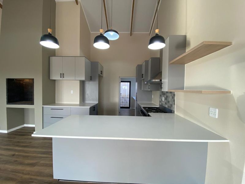 Modern kitchen featuring sleek grey cabinetry, stone countertops, built-in appliances, and a feature fireplace, set within an open-plan living space with high ceilings.