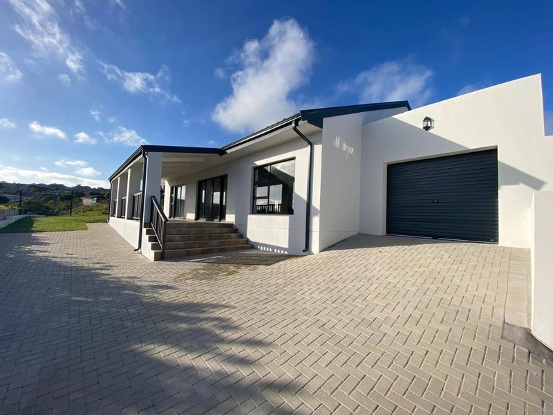 Modern single-story residence featuring a paved driveway, integrated garage, and a covered patio area with clean white exterior finishes.