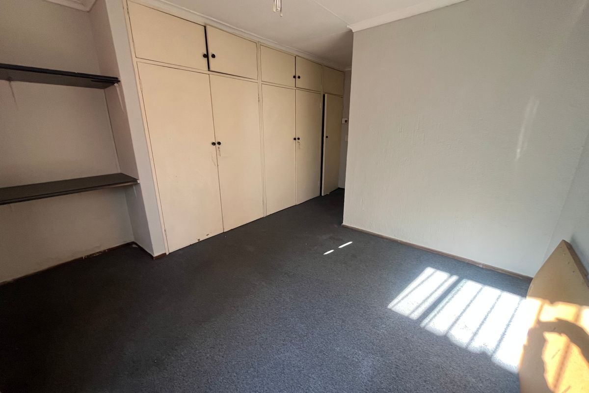 An empty bedroom featuring built-in cupboards, carpeted flooring, and a ceiling fan, offering a blank canvas for potential updates and personalization.