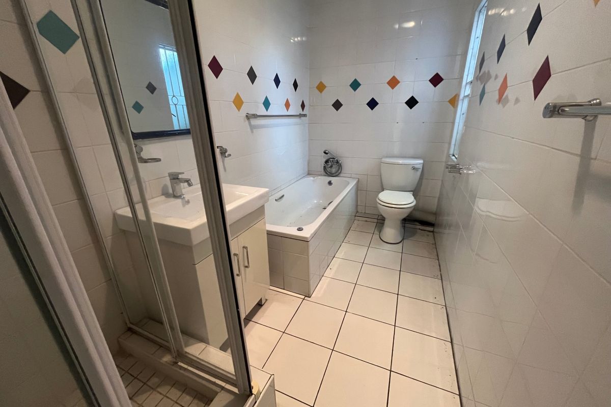 A functional bathroom featuring a shower enclosure, bathtub, vanity basin, and toilet, finished with white wall tiles and a decorative diamond pattern.