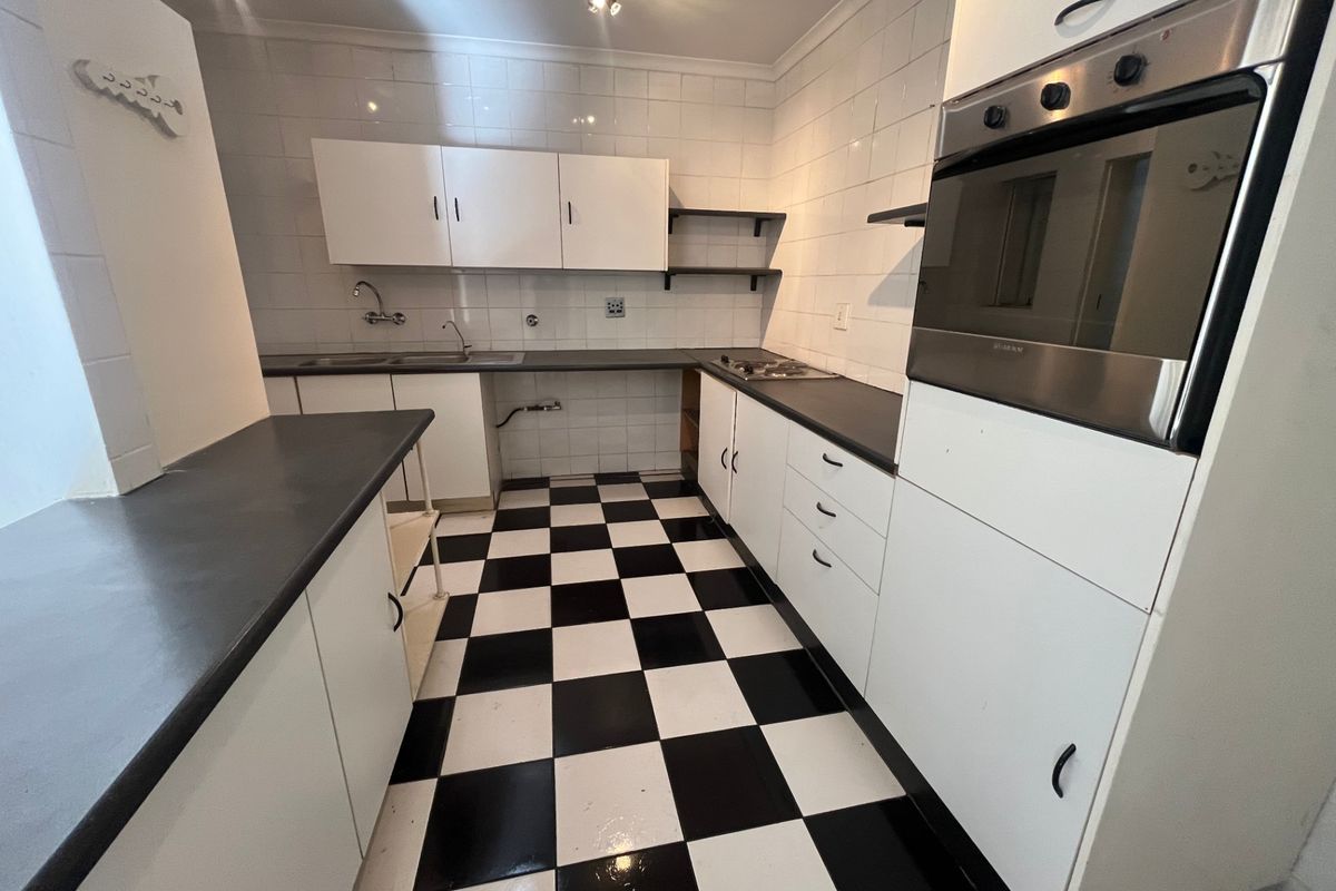 A functional kitchen featuring built-in oven, hob, double sink, and ample cabinetry with a classic black and white checkered floor.
