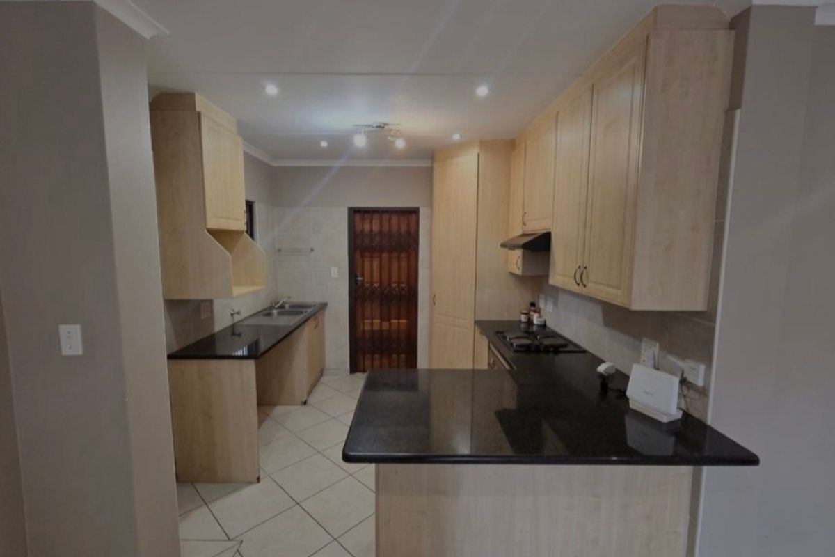A functional kitchen featuring light wood cabinetry, dark granite countertops, a gas hob with extractor fan, and tiled flooring.