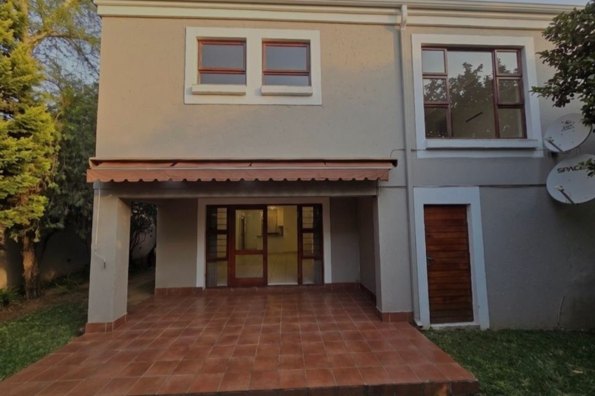 Rear view of the townhouse featuring a covered tiled patio, retractable awning, and established garden access.
