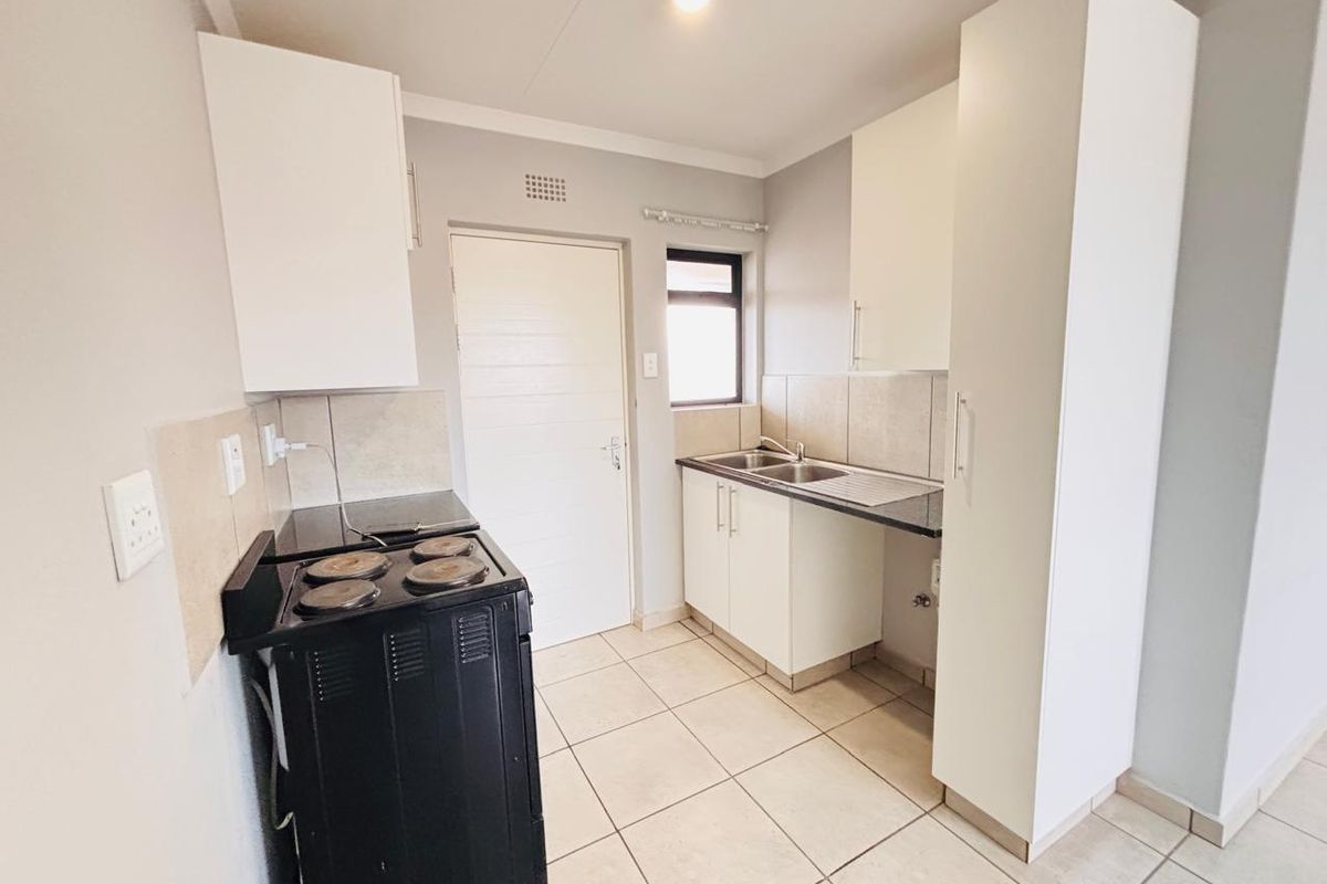 A functional kitchen featuring white built-in cabinetry, a double sink, tiled backsplash, and tiled flooring, offering a clean and practical workspace.