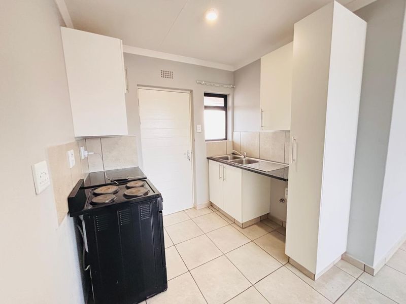 A functional kitchen featuring white built-in cabinetry, a double sink, tiled backsplash, and tiled flooring, offering a clean and practical workspace.