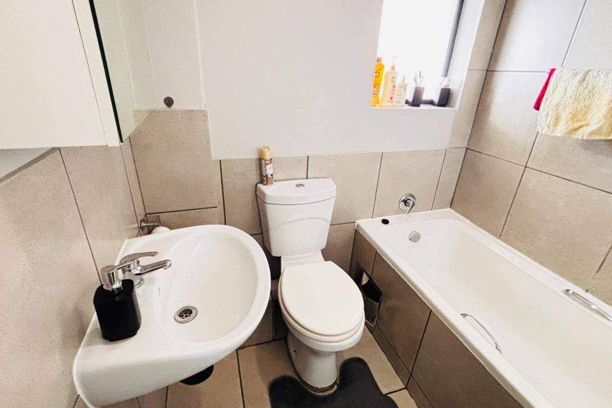 A functional bathroom featuring a pedestal washbasin, toilet, and bathtub with neutral wall and floor tiling.