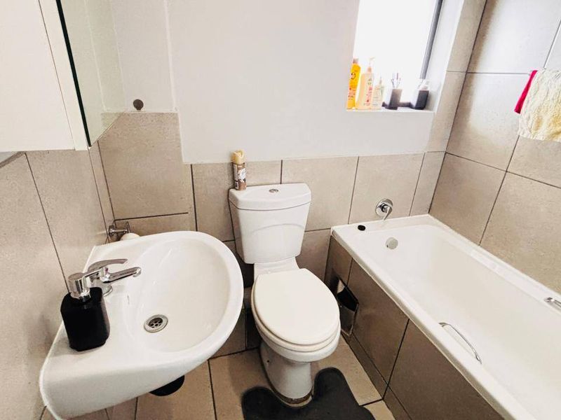 A functional bathroom featuring a pedestal washbasin, toilet, and bathtub with neutral wall and floor tiling.