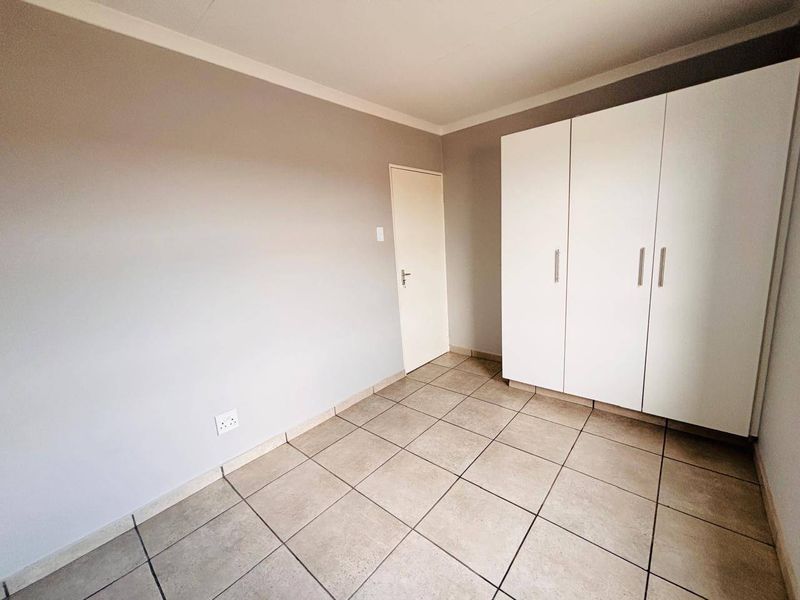 A clean, empty bedroom featuring neutral wall tones, tiled flooring, and a white built-in wardrobe.