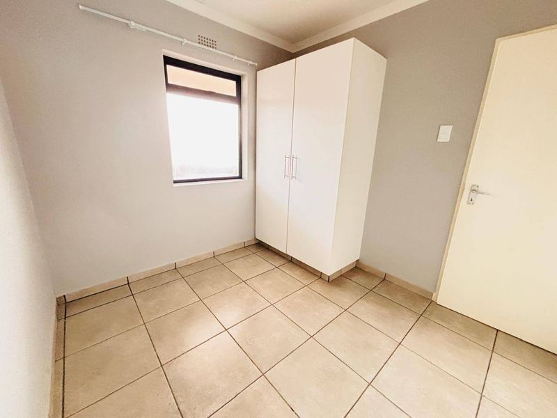 A clean, empty bedroom featuring neutral tiled flooring, a built-in wardrobe, and a window with a curtain rail.