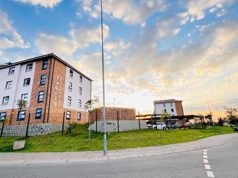 Exterior view of the Riverstone Eagles apartment complex, featuring brick facade architecture, landscaped grounds, and paved access areas at sunset.