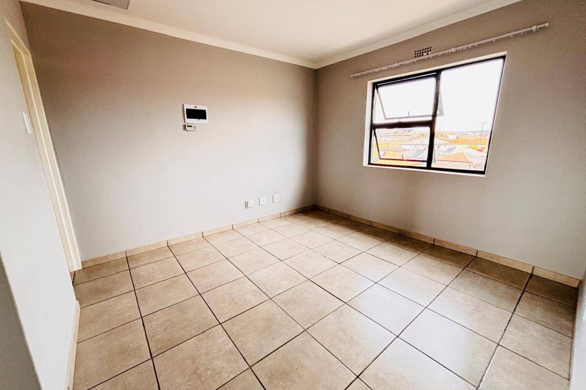A bright, empty bedroom featuring neutral wall paint, tiled flooring, and an aluminium-framed window with a view of the surrounding area.