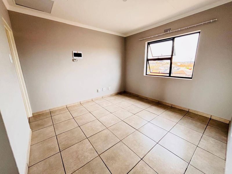 A bright, empty bedroom featuring neutral wall paint, tiled flooring, and an aluminium-framed window with a view of the surrounding area.