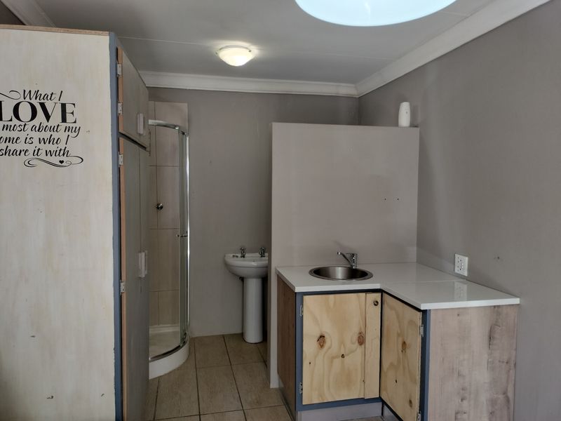 A functional bathroom space featuring a shower enclosure, pedestal basin, and a small kitchenette area with built-in cabinetry and sink.