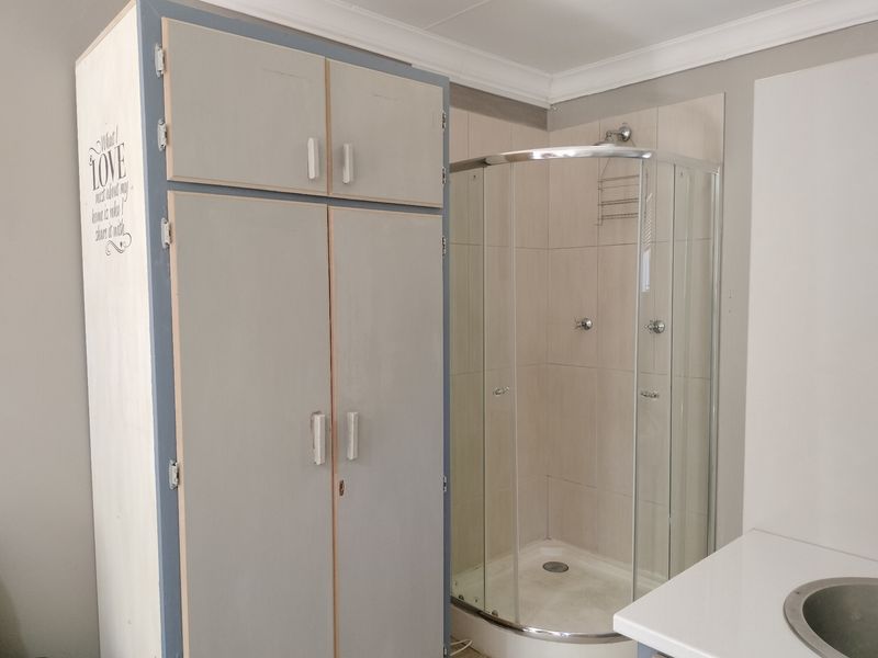 A functional bathroom featuring a corner shower enclosure, built-in storage cabinetry, and a vanity basin with neutral wall tiling.