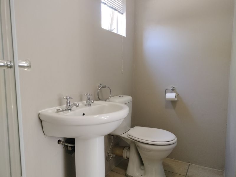 A functional bathroom featuring a white pedestal washbasin and a dual-flush toilet with neutral wall finishes and tiled flooring.