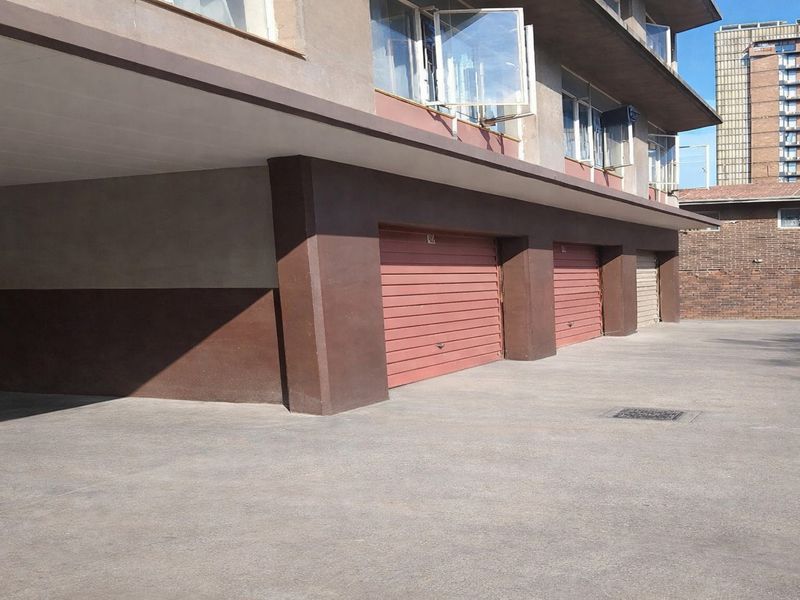 Exterior view of the apartment building featuring a row of secure, roll-up garage doors and a paved driveway area.