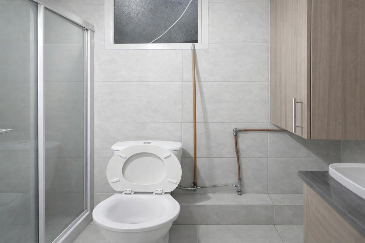 A functional bathroom featuring a shower enclosure, toilet, and vanity cabinet with exposed copper plumbing fixtures.