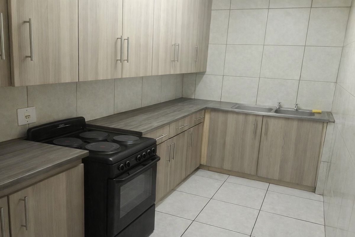 A functional kitchen featuring light wood-grain cabinetry, laminate countertops, tiled splashbacks, a double-basin sink, and a freestanding electric stove.