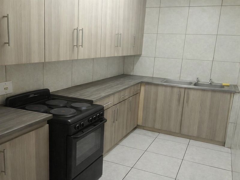 A functional kitchen featuring light wood-grain cabinetry, laminate countertops, tiled splashbacks, a double-basin sink, and a freestanding electric stove.