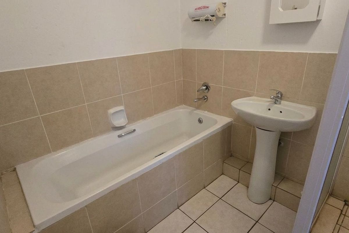 A functional bathroom featuring a bathtub, pedestal sink, and separate shower enclosure with neutral wall and floor tiling.