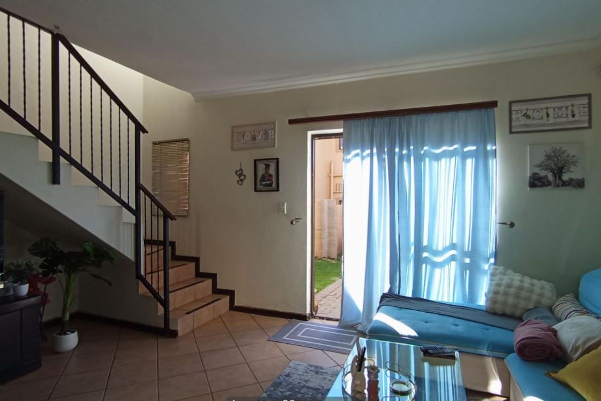 A living room featuring tiled flooring, a staircase with a metal balustrade, and direct access to the rear garden through a sliding door.