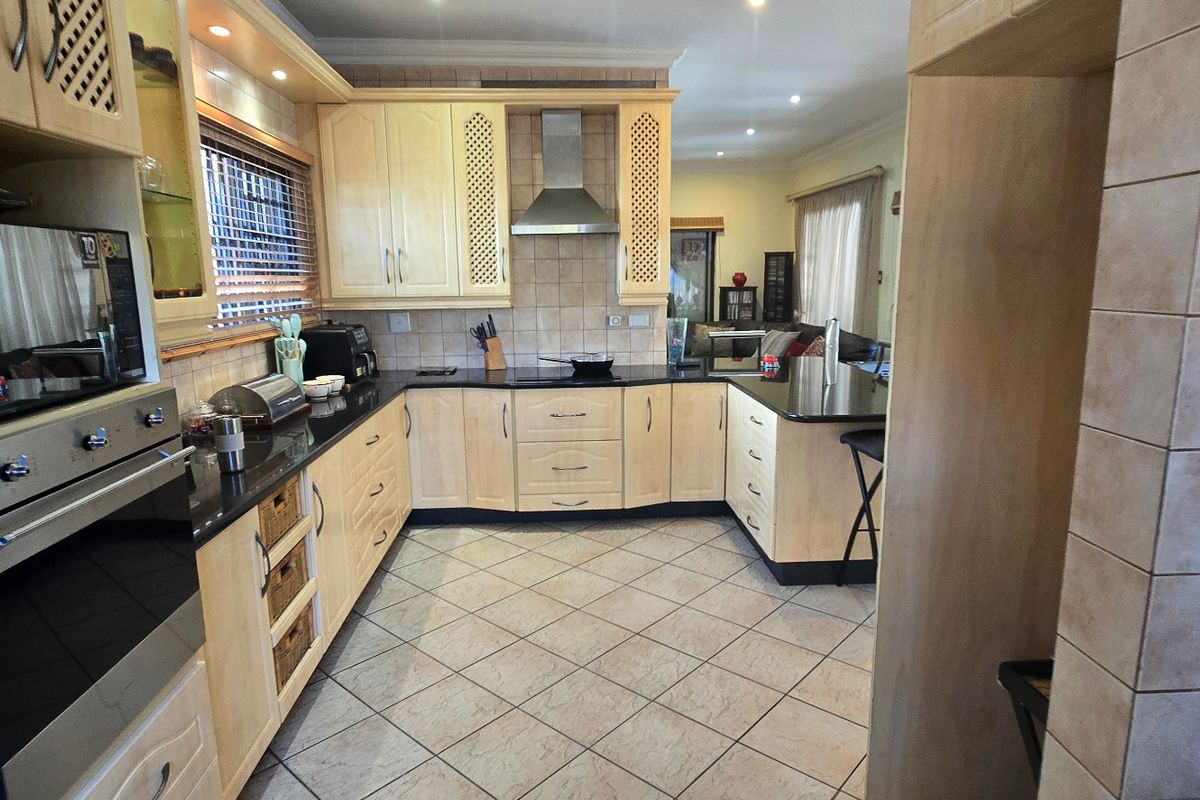 A functional kitchen featuring light wood cabinetry, granite countertops, built-in oven, extractor fan, and tiled flooring, with an open-plan layout leading to the living area.