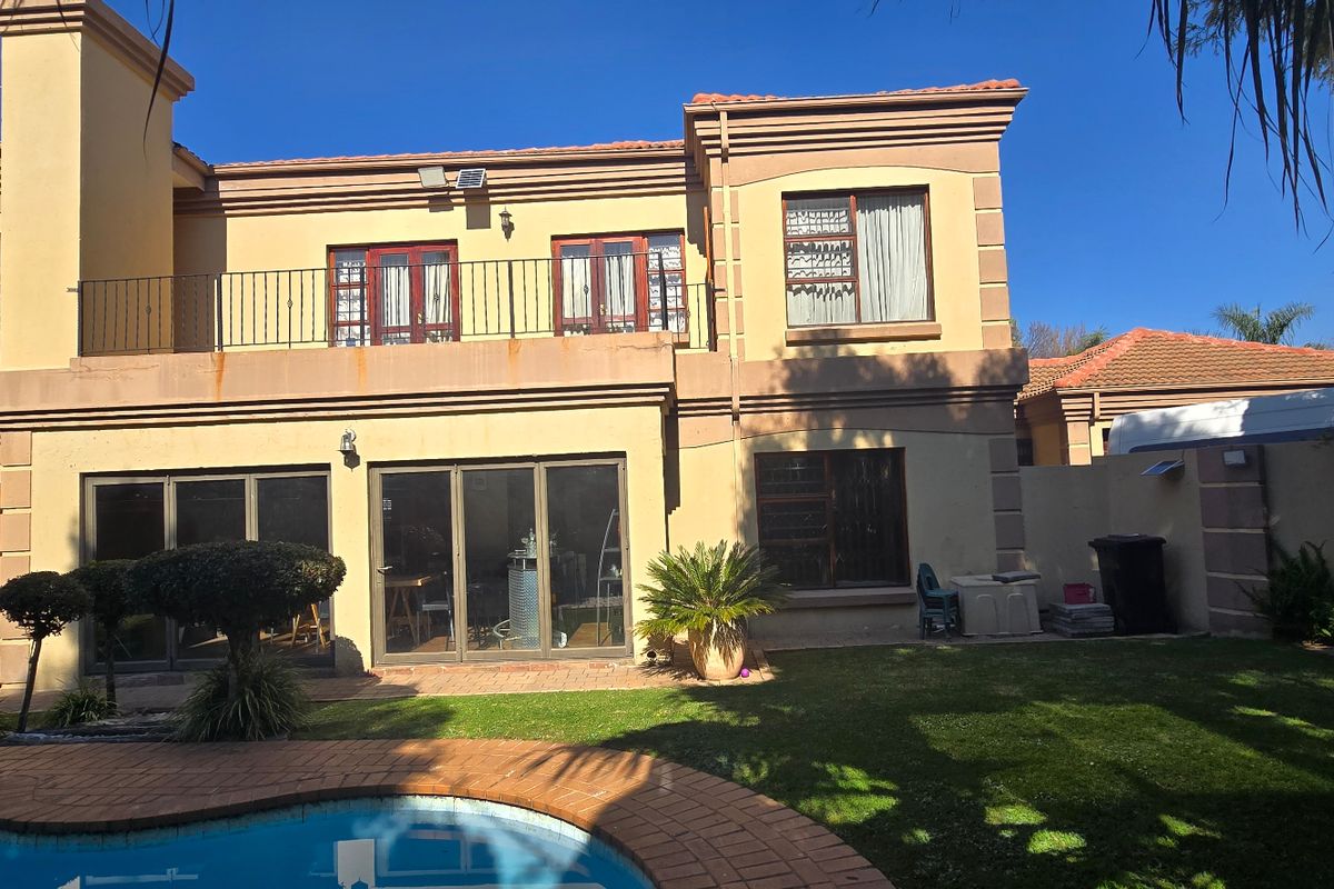 Rear view of a two-story house featuring a swimming pool, brick-paved patio area, and an upper-level balcony with wrought iron railings.