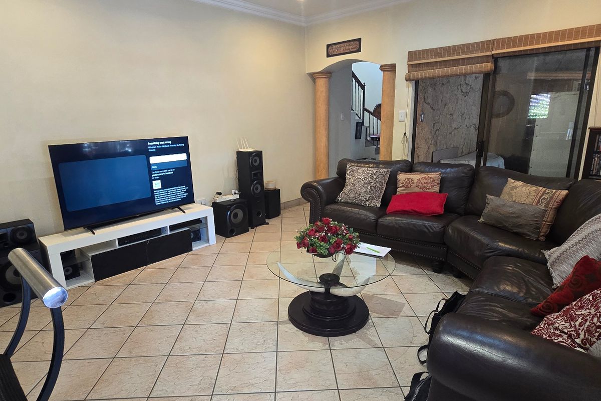 A spacious living room featuring ceramic tile flooring, decorative columns, and sliding glass door access to the exterior.