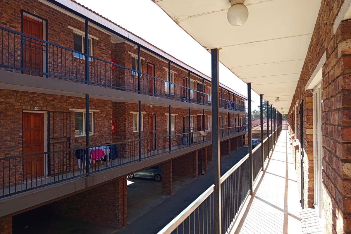 Exterior view of an apartment complex featuring a long covered walkway, exposed brick facade, and metal balustrades along the upper levels.