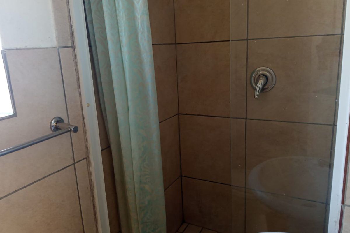A functional bathroom shower area featuring tiled walls, a glass screen, and a chrome mixer tap.