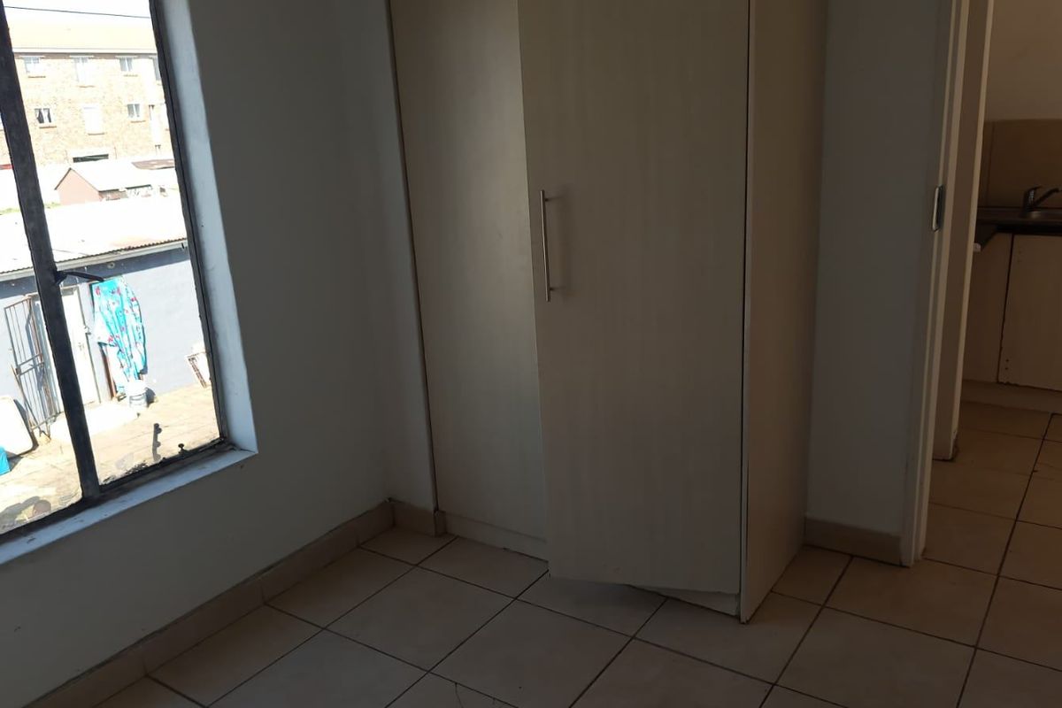 A simple bedroom featuring tiled flooring and a built-in wardrobe, with a view overlooking the exterior area.