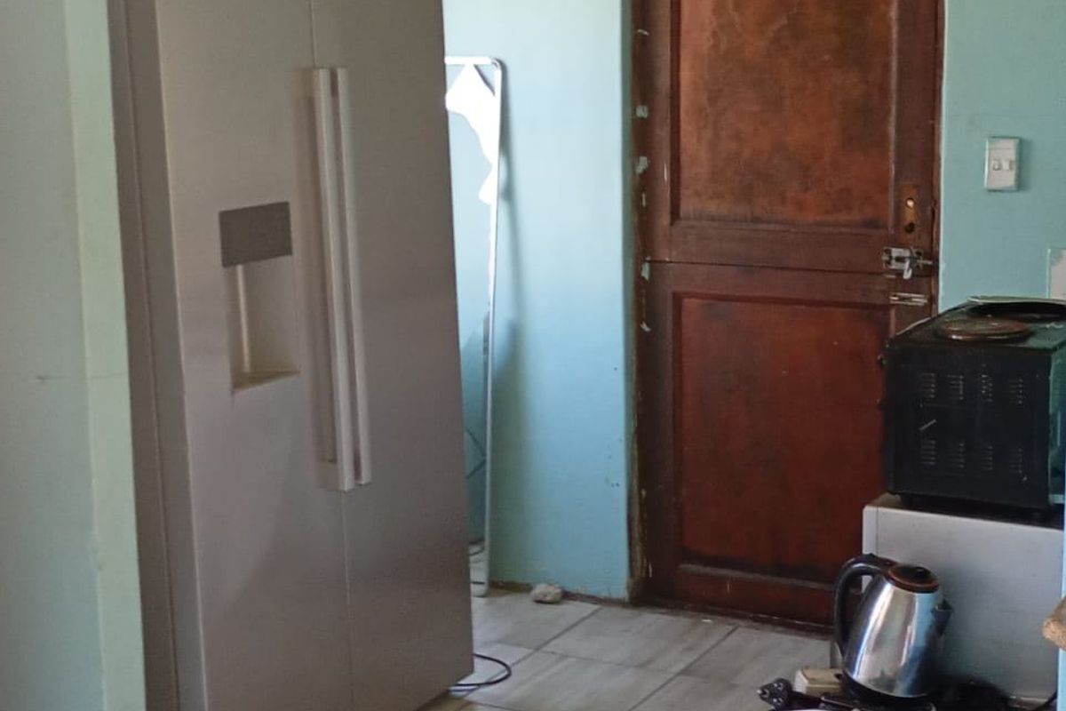A kitchen area featuring tiled flooring and a wooden door, currently showing signs of wear and requiring cosmetic updates to improve the space.