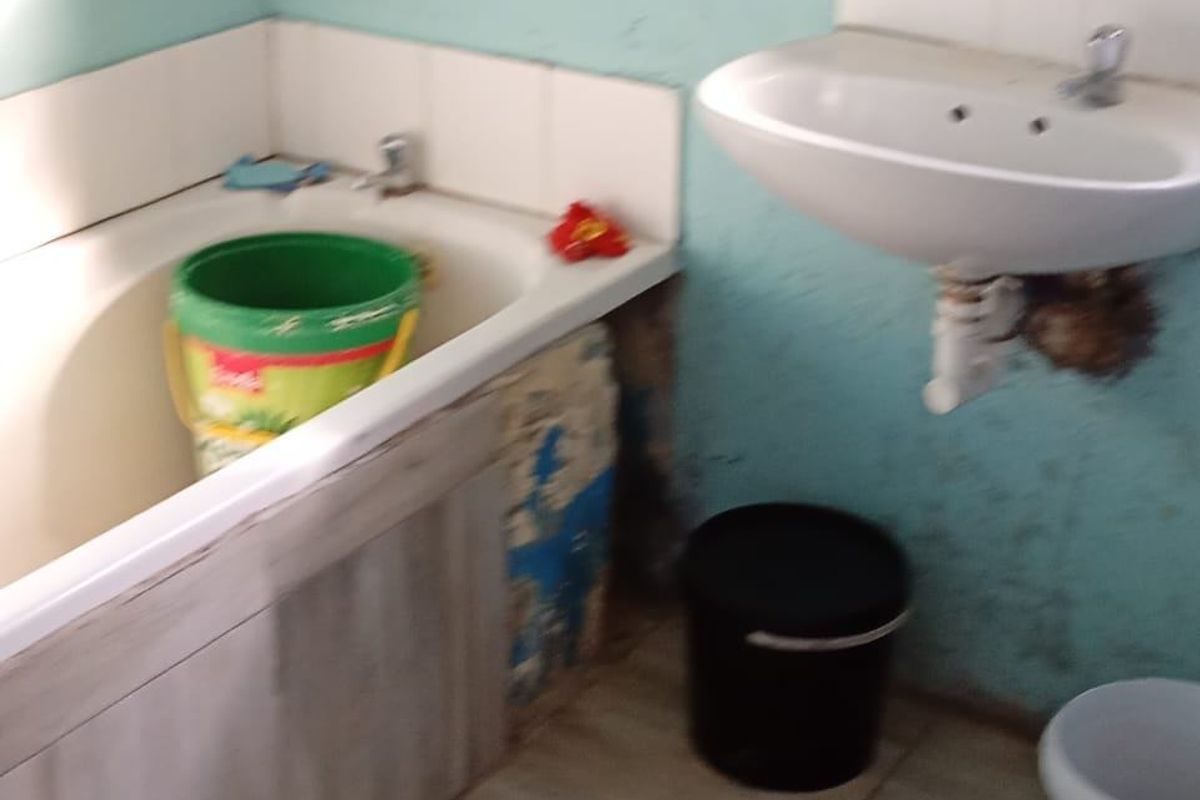 A bathroom featuring a bathtub and wall-mounted basin, currently requiring significant maintenance and repair to the wall finishes and bathtub surround.