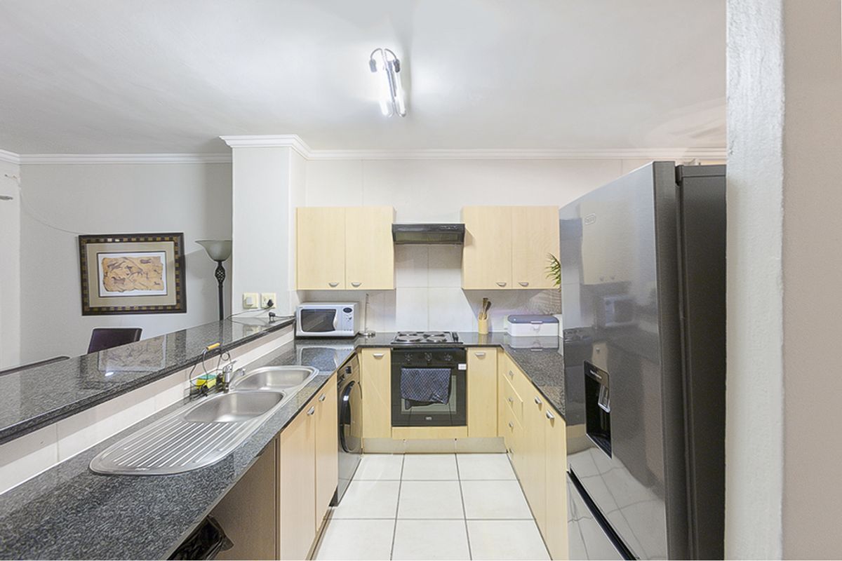 A functional kitchen featuring light wood cabinetry, granite countertops, a double sink, and built-in oven with extractor fan.