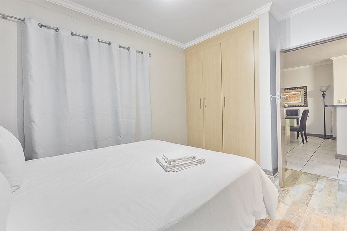 A bedroom featuring built-in wooden cupboards, crown molding, and wood-look flooring, with an open doorway leading to an adjacent living area.