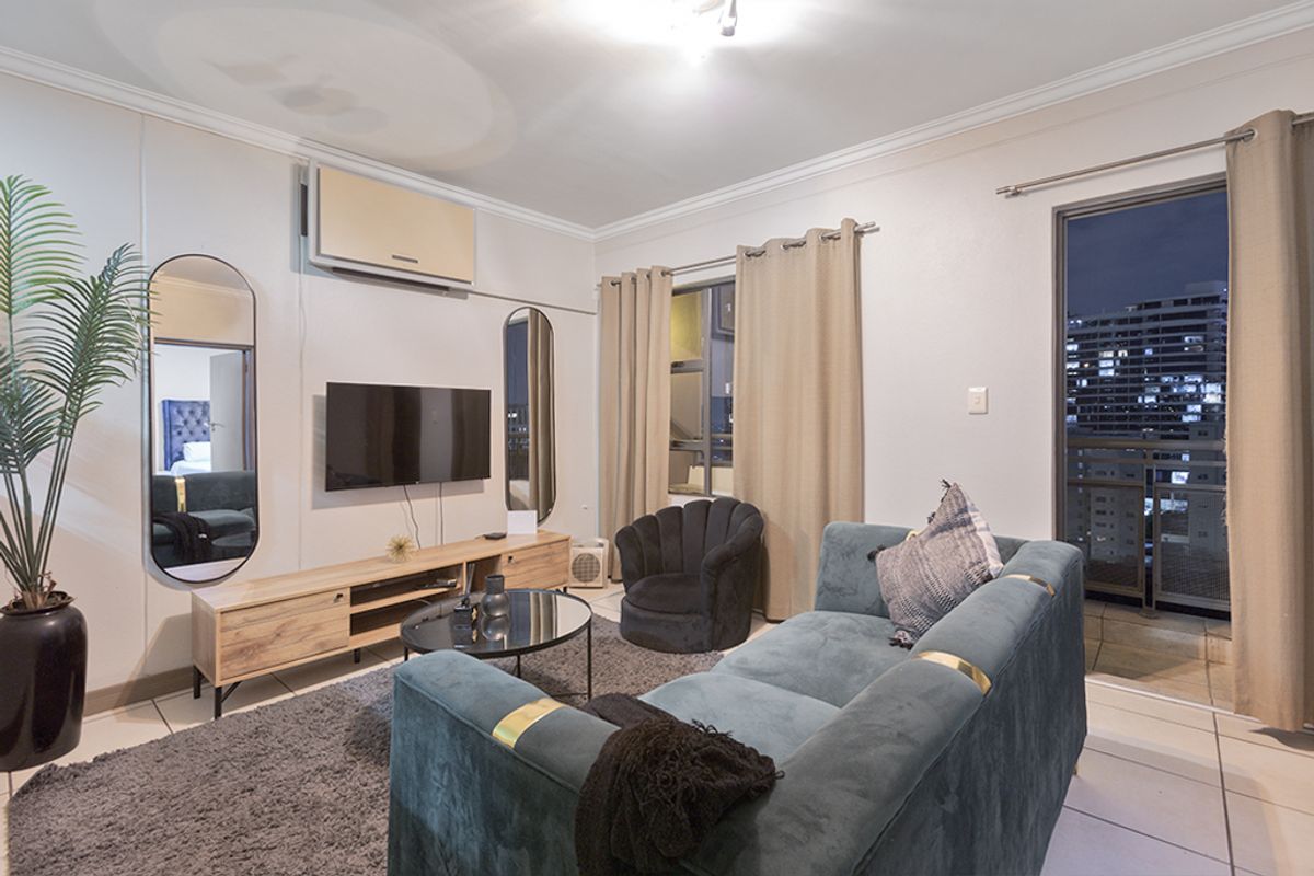 A well-maintained living room featuring tiled flooring, crown molding, a wall-mounted air conditioning unit, and direct access to a private balcony.