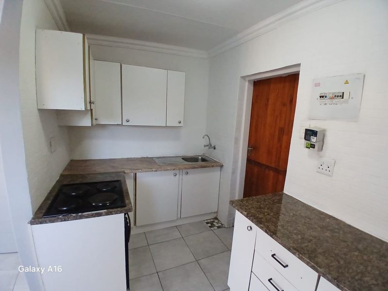 Compact kitchen featuring white cabinetry, laminate countertops, an electric hob, and tiled flooring. The space is functional but requires cosmetic updates.