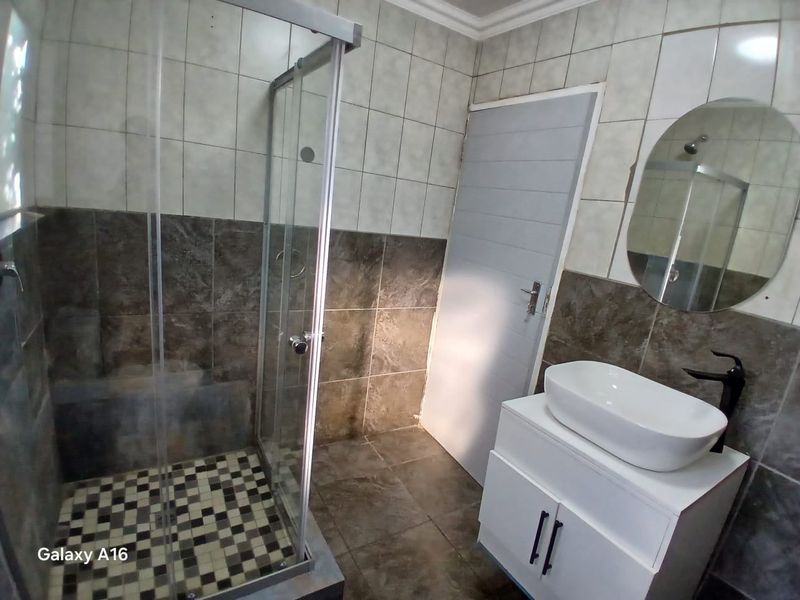 Modern bathroom featuring a glass shower enclosure, a contemporary vanity with a vessel sink, and stylish two-tone wall tiling.