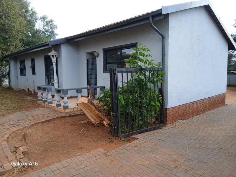 Front exterior view of the house featuring a paved driveway, a small tiled patio with concrete balustrades, and a metal security gate.