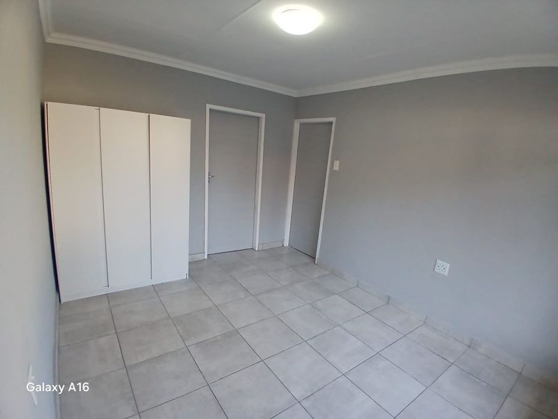 A clean, empty bedroom featuring neutral grey walls, tiled flooring, and a built-in wardrobe, offering a blank canvas for personalization.