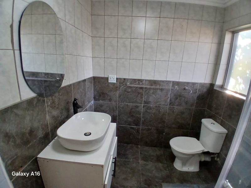 A clean, modern bathroom featuring a vessel sink on a vanity cabinet, a wall-mounted mirror, and a standard toilet with tiled finishes.