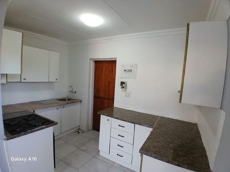 A functional kitchen featuring white built-in cabinetry, laminate countertops, a stainless steel sink, and an integrated electric hob with tiled flooring.