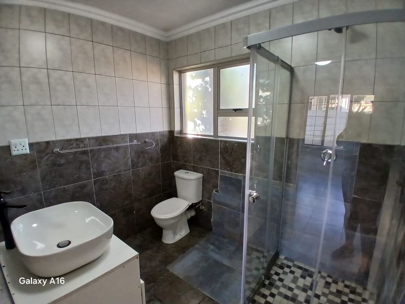 A modern bathroom featuring a vessel sink, a toilet, and a glass-enclosed shower with tiled walls and flooring.