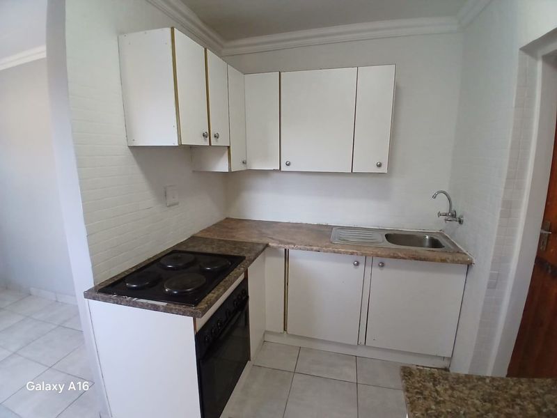 A compact, functional kitchen featuring white cabinetry, a laminate countertop, an electric hob, and a stainless steel sink with tiled flooring.