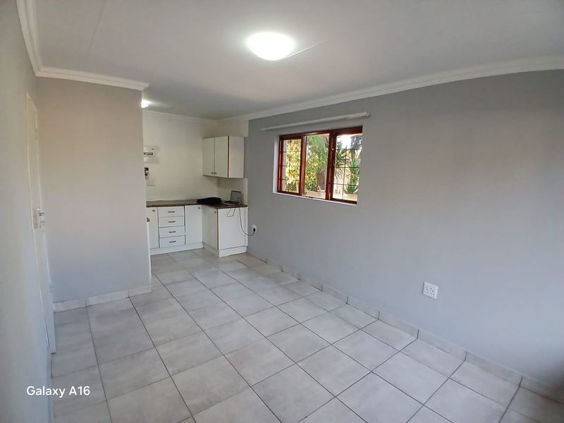 An open-plan living and kitchen area featuring neutral grey walls, tiled flooring, and functional built-in cabinetry.