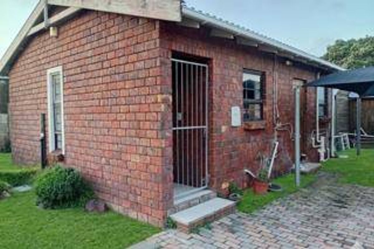 Rear view of a face brick house featuring a paved walkway, security gate, and external plumbing fixtures.