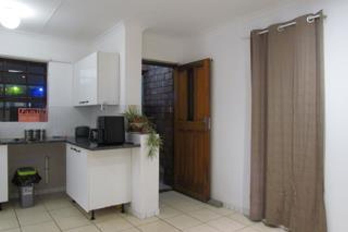 A functional kitchen area featuring white cabinetry, dark countertops, tiled flooring, and direct access to an exterior space via a timber door.