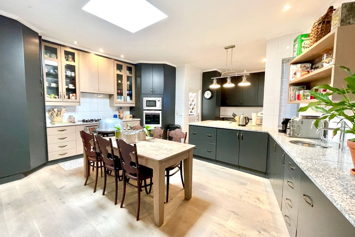 Spacious modern kitchen featuring dark cabinetry, granite countertops, integrated appliances, a large central dining area, and a bright skylight.